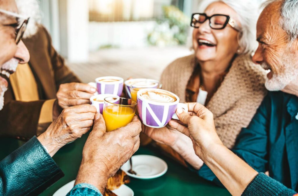 A group of seniors cheers mugs of coffee (and one orange juice) together in celebration of their home in senior living